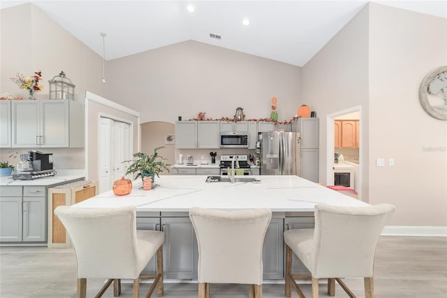 kitchen with stainless steel appliances, gray cabinets, a kitchen island with sink, and light hardwood / wood-style flooring