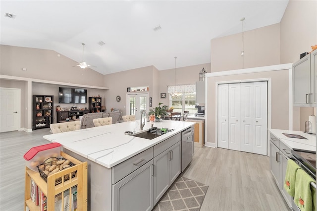 kitchen with stainless steel appliances, vaulted ceiling, hanging light fixtures, sink, and a kitchen island with sink