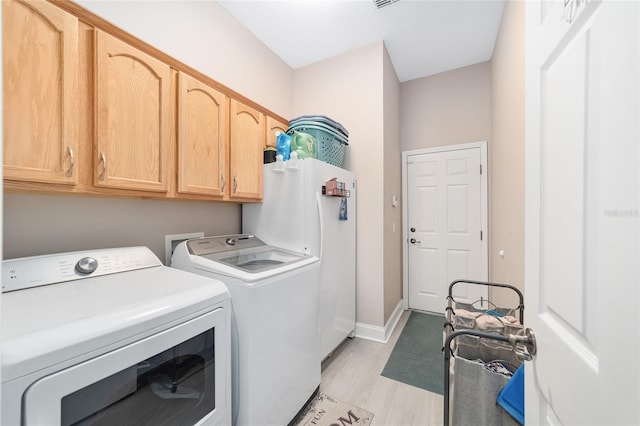 clothes washing area featuring light hardwood / wood-style floors, washing machine and dryer, and cabinets