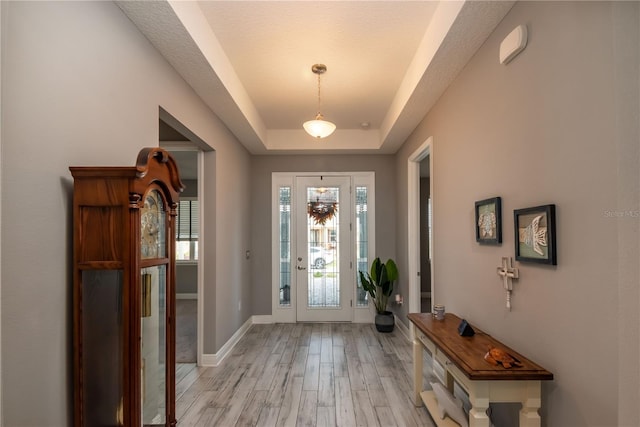 entryway with light wood-type flooring, a tray ceiling, and a textured ceiling