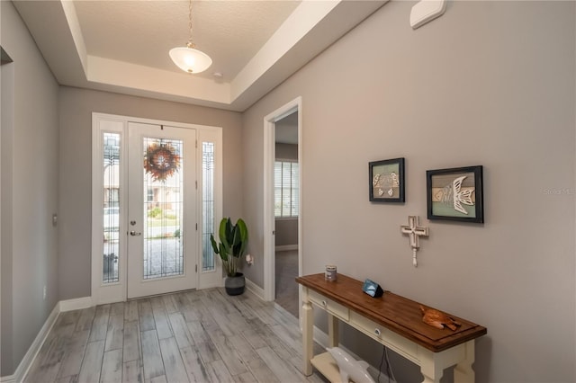 entryway with a textured ceiling, light wood-type flooring, and a tray ceiling