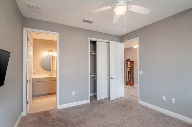 unfurnished bedroom featuring ceiling fan, connected bathroom, light carpet, and a closet