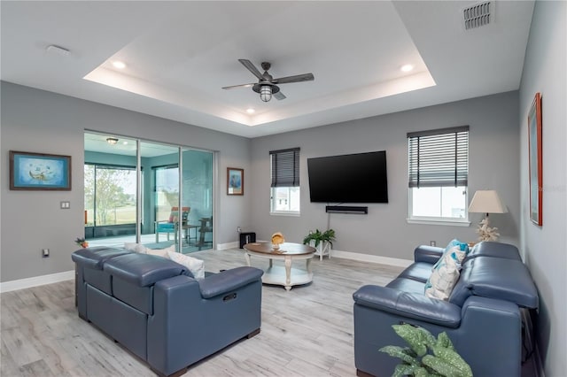 living room featuring ceiling fan, light wood-type flooring, and a tray ceiling