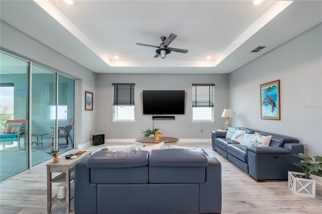 living room featuring light wood-type flooring, a wealth of natural light, and a raised ceiling