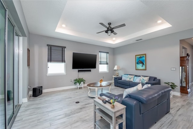 living room with a wealth of natural light, light hardwood / wood-style flooring, and a tray ceiling