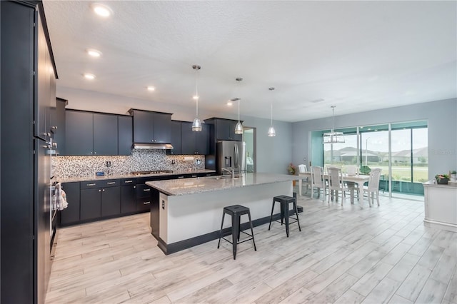 kitchen featuring an island with sink, light hardwood / wood-style floors, decorative light fixtures, and stainless steel appliances