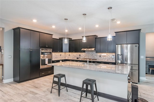 kitchen with a center island with sink, a breakfast bar, appliances with stainless steel finishes, pendant lighting, and light wood-type flooring