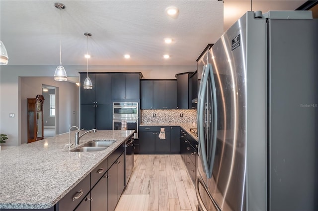 kitchen featuring stainless steel appliances, sink, a spacious island, light hardwood / wood-style flooring, and decorative light fixtures