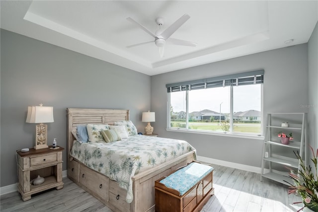 bedroom featuring light hardwood / wood-style flooring, ceiling fan, and a raised ceiling