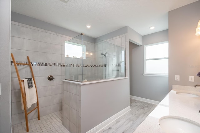 bathroom featuring hardwood / wood-style floors, vanity, a textured ceiling, and a tile shower