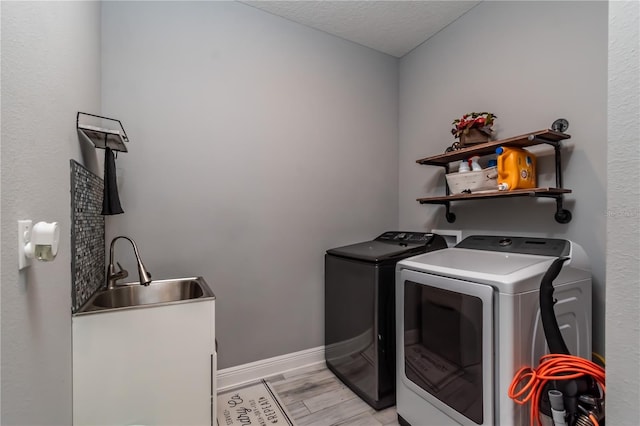 laundry area with a textured ceiling, washing machine and dryer, sink, and light hardwood / wood-style flooring