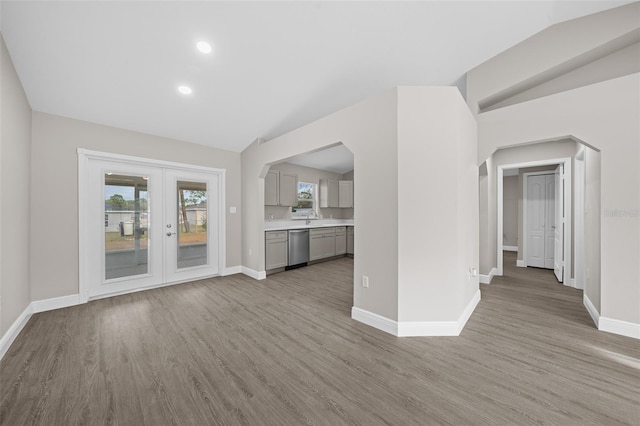 unfurnished living room featuring french doors, light wood-type flooring, lofted ceiling, and sink