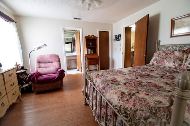 bedroom with ensuite bath, light hardwood / wood-style flooring, and a textured ceiling