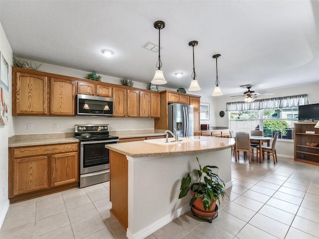 kitchen with appliances with stainless steel finishes, ceiling fan, light tile patterned floors, pendant lighting, and a center island with sink