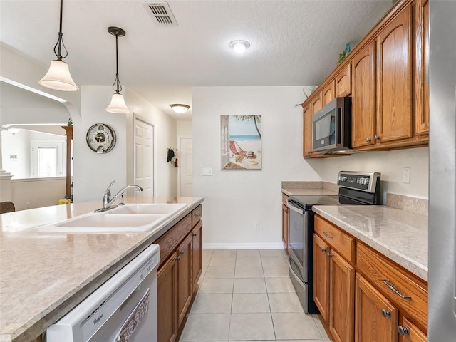 kitchen featuring sink, hanging light fixtures, a textured ceiling, light tile patterned floors, and appliances with stainless steel finishes