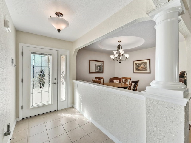 entryway with a chandelier, light tile patterned floors, a textured ceiling, and ornate columns