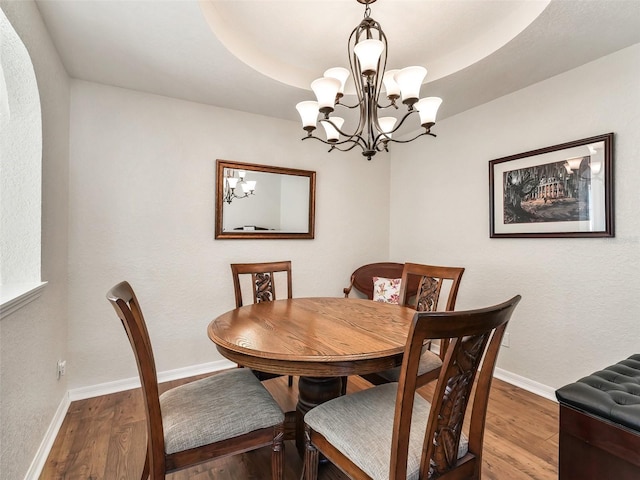 dining space with hardwood / wood-style floors, a raised ceiling, and a notable chandelier