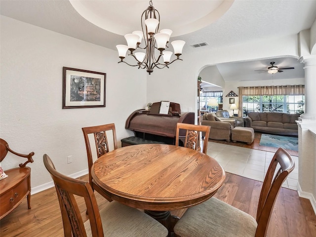 dining room featuring a raised ceiling, ceiling fan with notable chandelier, hardwood / wood-style flooring, and ornate columns