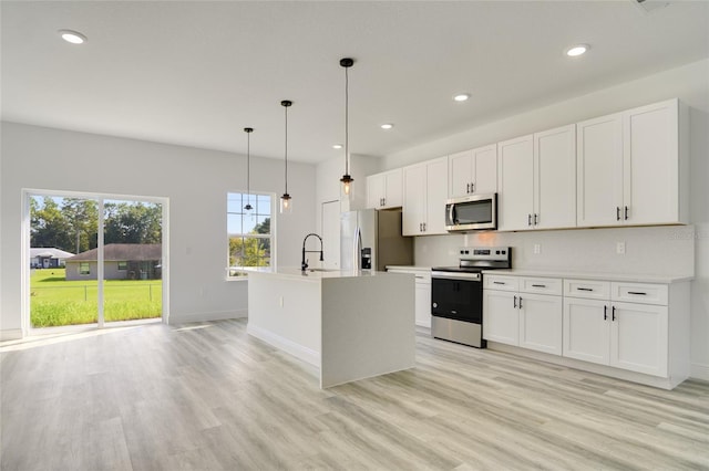 kitchen featuring stainless steel appliances, a center island with sink, white cabinets, light wood-type flooring, and decorative light fixtures