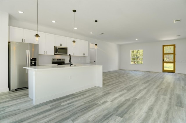 kitchen with white cabinetry, appliances with stainless steel finishes, light hardwood / wood-style floors, and a kitchen island with sink