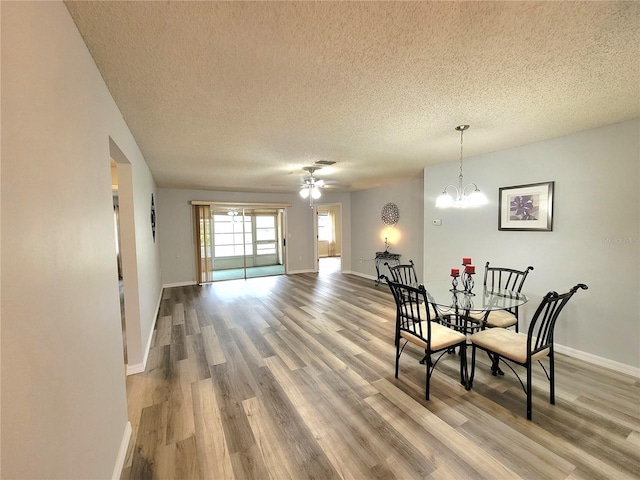 dining space featuring hardwood / wood-style floors, ceiling fan with notable chandelier, and a textured ceiling