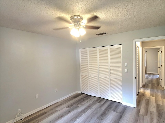 unfurnished bedroom featuring a closet, a textured ceiling, hardwood / wood-style flooring, and ceiling fan