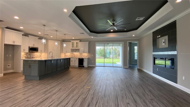 kitchen with a tray ceiling, stainless steel microwave, open floor plan, white cabinets, and an island with sink