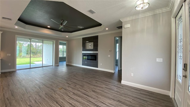 unfurnished living room with ceiling fan, dark hardwood / wood-style flooring, crown molding, and a tray ceiling