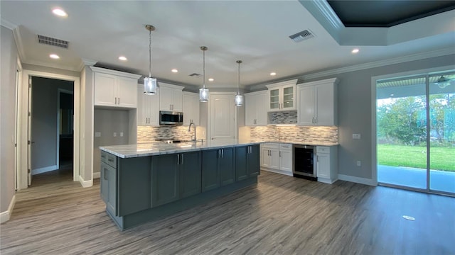 kitchen featuring a center island with sink, crown molding, wine cooler, decorative light fixtures, and white cabinetry