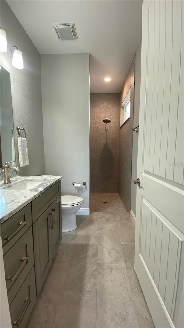 bathroom with a tile shower, vanity, and toilet