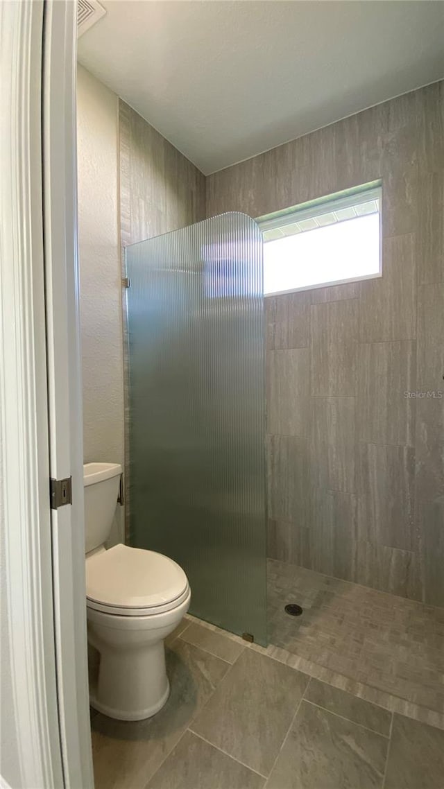 bathroom featuring tile patterned flooring, toilet, and tiled shower