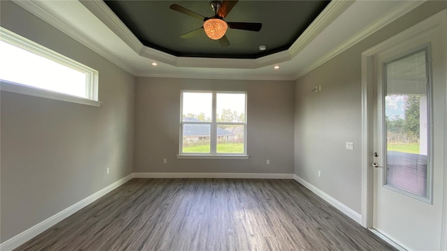 empty room with dark wood finished floors, a raised ceiling, crown molding, and baseboards