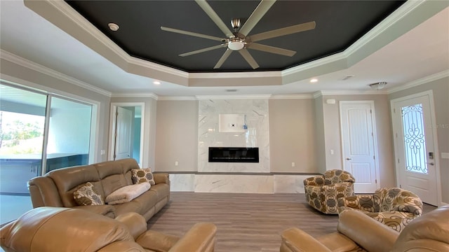 living area with recessed lighting, a raised ceiling, a premium fireplace, ornamental molding, and ceiling fan