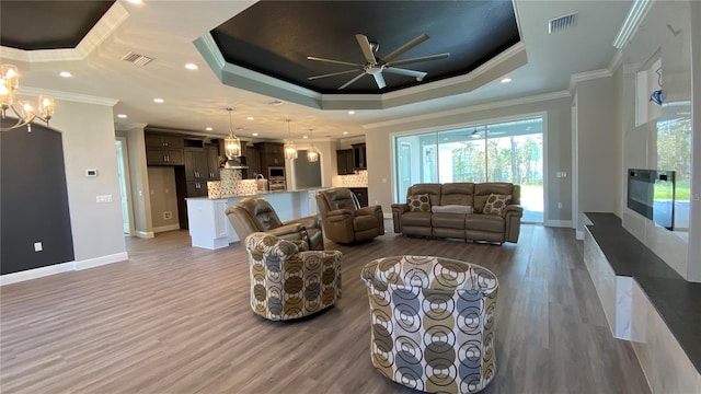 living area with a tray ceiling, visible vents, and wood finished floors