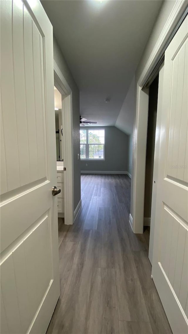 hallway featuring baseboards, vaulted ceiling, and dark wood-type flooring