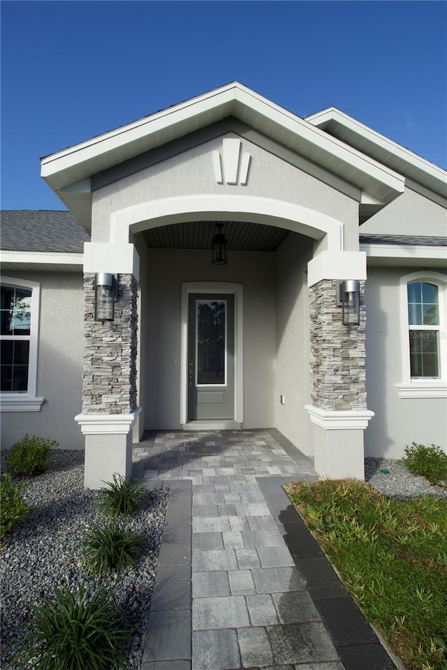 property entrance featuring stone siding, roof with shingles, and stucco siding