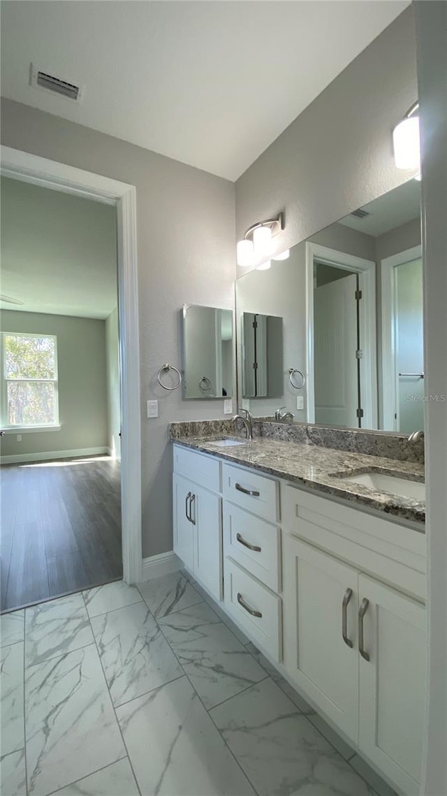 full bathroom with double vanity, marble finish floor, baseboards, and a sink