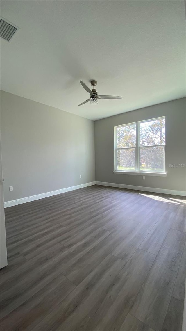 empty room featuring dark wood-style floors, baseboards, visible vents, and ceiling fan