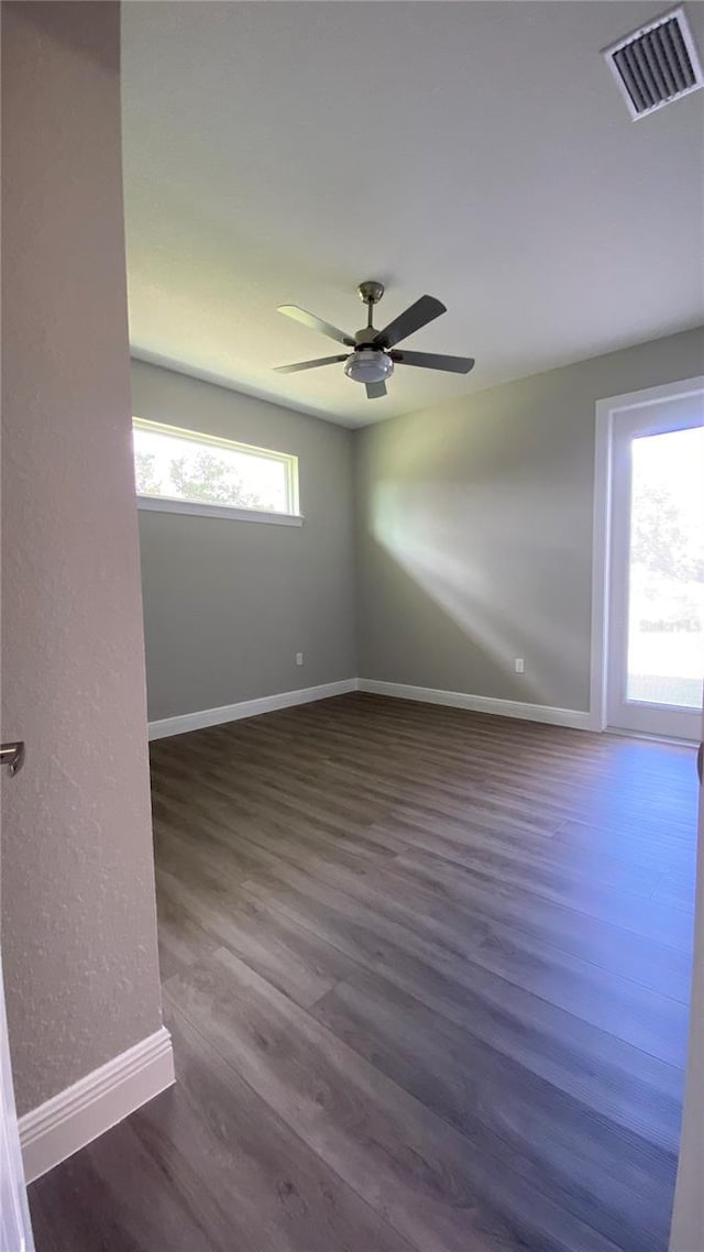 unfurnished room featuring a ceiling fan, dark wood finished floors, visible vents, and baseboards