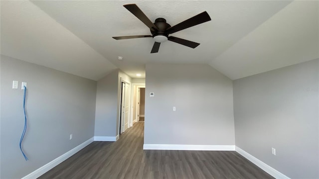 additional living space featuring dark wood-type flooring, lofted ceiling, baseboards, and a ceiling fan