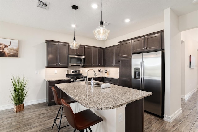 kitchen with stainless steel appliances, sink, an island with sink, and light stone countertops