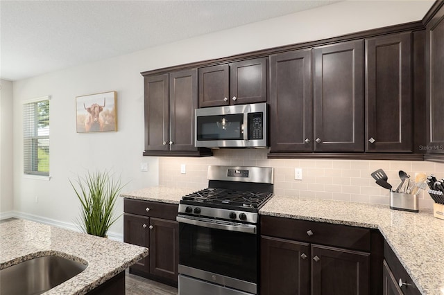 kitchen with dark brown cabinets, appliances with stainless steel finishes, tasteful backsplash, and light stone countertops