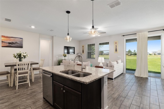 kitchen with hanging light fixtures, sink, an island with sink, dark hardwood / wood-style floors, and light stone countertops