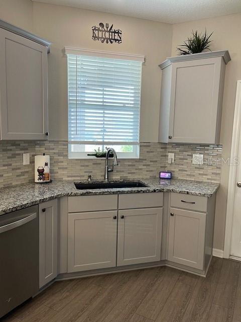 kitchen with backsplash, light stone countertops, sink, dark wood-type flooring, and stainless steel dishwasher