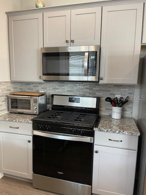 kitchen featuring tasteful backsplash, white cabinetry, appliances with stainless steel finishes, and light stone counters