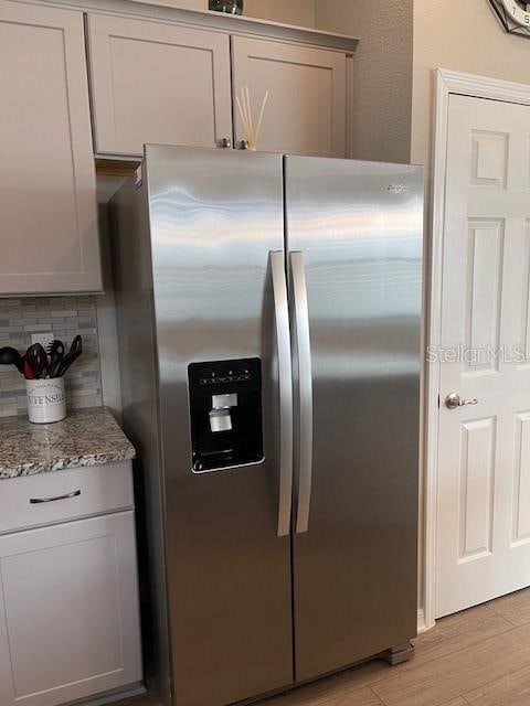 kitchen featuring light stone countertops, backsplash, light hardwood / wood-style flooring, gray cabinets, and stainless steel fridge