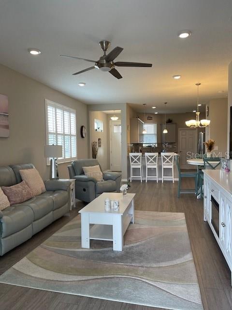 living room with dark wood-type flooring and ceiling fan with notable chandelier