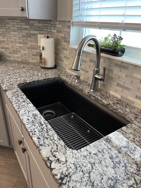 room details with backsplash, sink, light stone countertops, and white cabinets