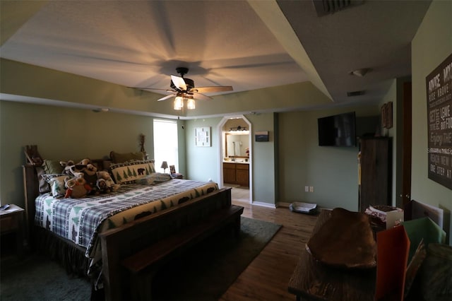 bedroom with connected bathroom, dark wood-type flooring, a tray ceiling, and ceiling fan