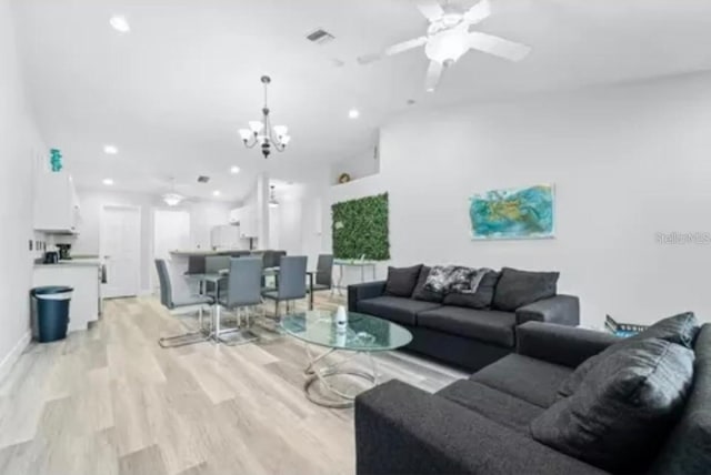 living room with light wood-type flooring and ceiling fan with notable chandelier